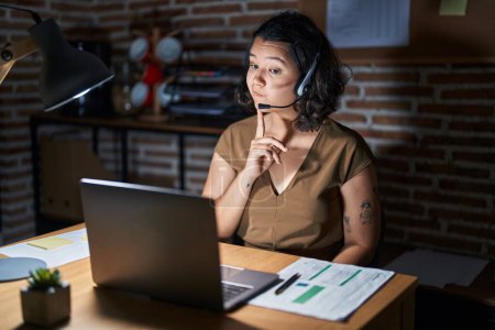Photo for Young hispanic woman working at the office at night thinking concentrated about doubt with finger on chin and looking up wondering - Royalty Free Image