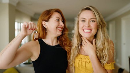 Foto de Dos mujeres sonriendo confiadas sosteniendo la llave de un nuevo hogar en casa - Imagen libre de derechos