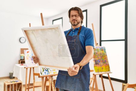 Téléchargez les photos : Moyen Age caucasien homme souriant confiant regarder dessiner toile au studio d'art - en image libre de droit