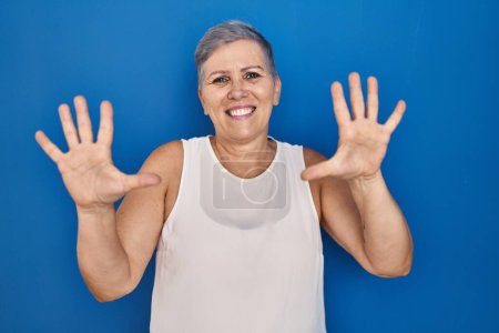 Photo for Middle age caucasian woman standing over blue background showing and pointing up with fingers number ten while smiling confident and happy. - Royalty Free Image