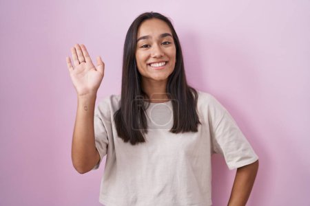 Téléchargez les photos : Jeune femme hispanique debout sur fond rose renonçant à dire bonjour heureux et souriant, geste de bienvenue amical - en image libre de droit