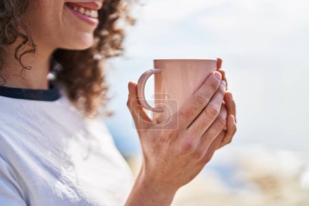 Téléchargez les photos : Young hispanic woman smiling confident drinking coffee at seaside - en image libre de droit
