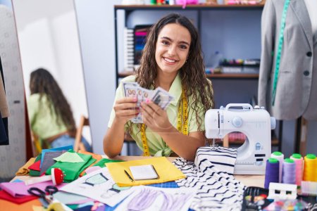 Photo for Young beautiful hispanic woman tailor smiling confident holding dollars at clothing factory - Royalty Free Image