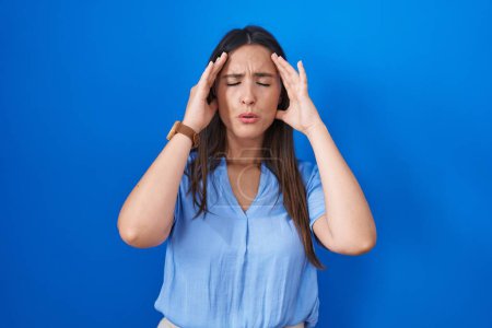 Photo for Young brunette woman standing over blue background with hand on head, headache because stress. suffering migraine. - Royalty Free Image