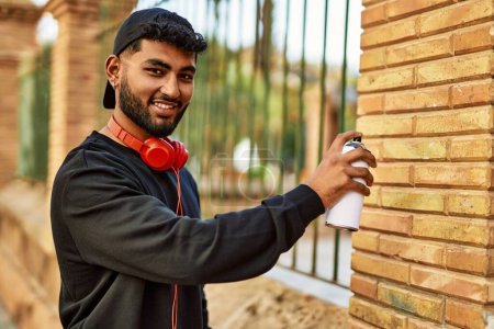 Téléchargez les photos : Jeune homme arabe souriant graffiti peinture confiant à la rue - en image libre de droit