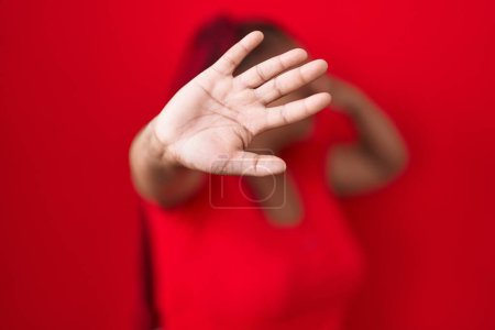 Photo for African american woman with braided hair standing over red background covering eyes with hands and doing stop gesture with sad and fear expression. embarrassed and negative concept. - Royalty Free Image