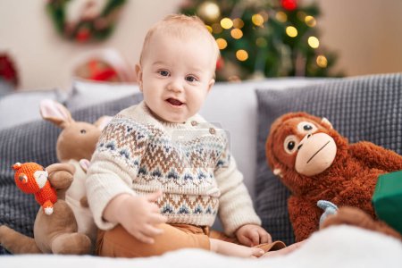 Photo for Adorable caucasian baby smiling confident sitting on sofa by christmas tree at home - Royalty Free Image