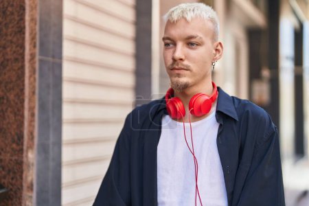 Foto de Joven hombre caucásico con auriculares con expresión seria en la calle - Imagen libre de derechos