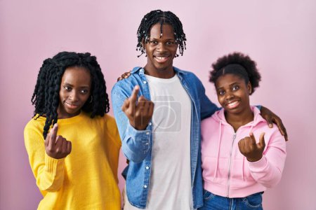 Foto de Grupo de tres jóvenes negros de pie juntos sobre fondo rosa señas vienen aquí gesto con la mano invitando a la bienvenida feliz y sonriente - Imagen libre de derechos