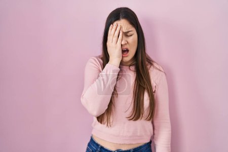 Photo for Young brunette woman standing over pink background yawning tired covering half face, eye and mouth with hand. face hurts in pain. - Royalty Free Image