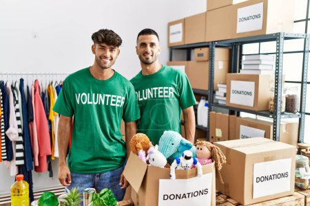 Photo for Young gay couple wearing volunteer t shirt at donations stand with a happy and cool smile on face. lucky person. - Royalty Free Image