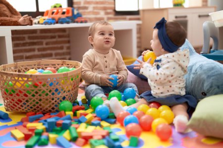 Foto de Dos niños pequeños jugando con bolas sentados en el suelo en el jardín de infantes - Imagen libre de derechos