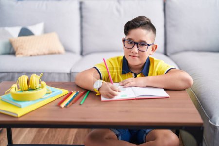 Téléchargez les photos : Adorable garçon hispanique dessin sur livre assis sur le sol à la maison - en image libre de droit