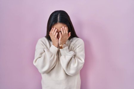 Foto de Joven mujer sudasiática de pie sobre fondo rosa con expresión triste cubriendo la cara con las manos mientras llora. concepto de depresión. - Imagen libre de derechos