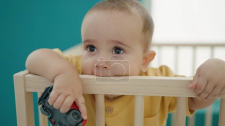 Photo for Adorable hispanic baby standing on cradle sucking wooden balustrade at bedroom - Royalty Free Image