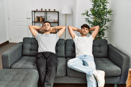Foto de Dos hombres hispanos pareja sonriendo confiado relajado con las manos en la cabeza en casa - Imagen libre de derechos