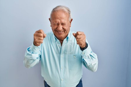 Téléchargez les photos : Homme âgé avec les cheveux gris debout sur fond bleu excité pour le succès avec les bras levés et les yeux fermés célébrant la victoire en souriant. concept gagnant. - en image libre de droit