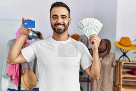 Foto de Joven cliente hispano con tarjeta de crédito y dólares comprando en tienda de ropa - Imagen libre de derechos
