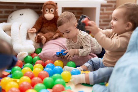 Foto de Dos niños adorables jugando con pelotas y coche sentado en el suelo en el jardín de infantes - Imagen libre de derechos