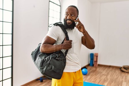 Junger afrikanisch-amerikanischer Mann mit Turntasche spricht im Sportzentrum auf dem Smartphone