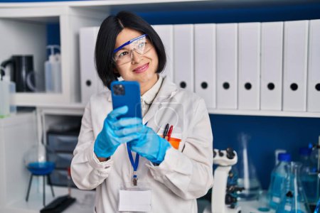 Photo for Young chinese woman scientist using smartphone working at laboratory - Royalty Free Image