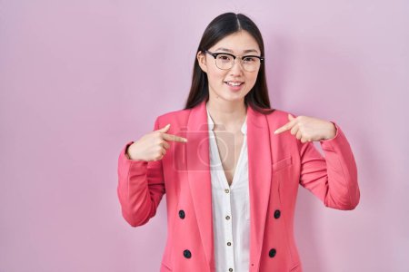 Foto de Mujer joven de negocios china con gafas que lucen confiadas con sonrisa en la cara, señalándose con los dedos orgullosos y felices. - Imagen libre de derechos
