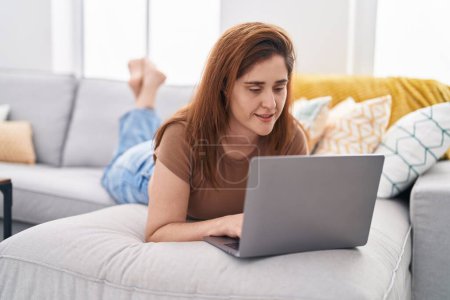 Téléchargez les photos : Jeune femme utilisant un ordinateur portable couché sur le canapé à la maison - en image libre de droit