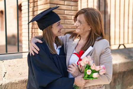 Téléchargez les photos : Mother and daughter hugging each other celebrating graduation holding diploma and flowers at university - en image libre de droit