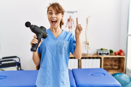 Photo for Beautiful caucasian woman holding therapy massage gun at wellness center surprised with an idea or question pointing finger with happy face, number one - Royalty Free Image