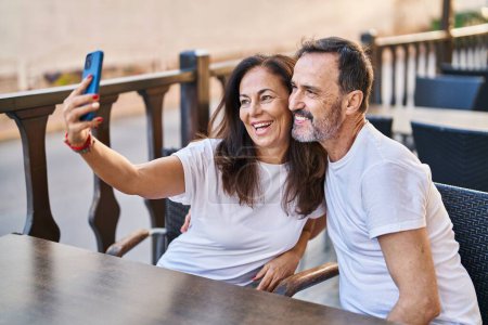 Foto de Mediana edad hombre y mujer pareja hacer selfie por el teléfono inteligente sentado en la mesa en la terraza de la cafetería - Imagen libre de derechos