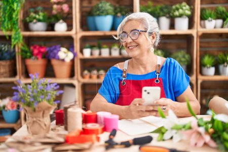 Photo for Middle age grey-haired woman florist smiling confident using smartphone at florist - Royalty Free Image