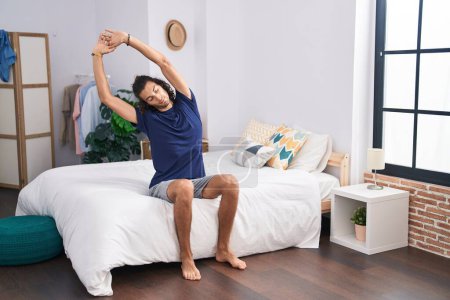 Photo for Young hispanic man waking up stretching arms at bedroom - Royalty Free Image
