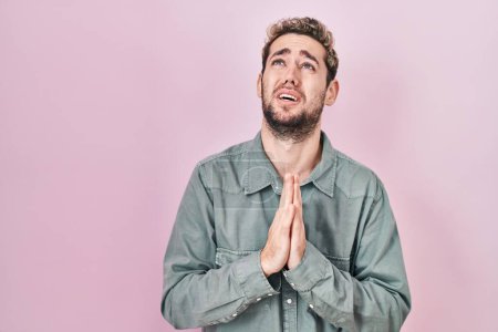 Téléchargez les photos : Hispanic man with beard standing over pink background begging and praying with hands together with hope expression on face very emotional and worried. begging. - en image libre de droit