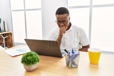 Téléchargez les photos : Jeune homme africain travaillant au bureau utilisant ordinateur portable se sentant mal et la toux comme symptôme de rhume ou de bronchite. concept de soins de santé. - en image libre de droit