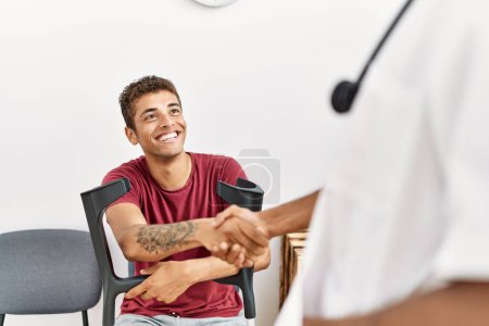 Téléchargez les photos : Deux hommes physiothérapeute et patient ayant une consultation médicale serrent la main à la salle d'attente de l'hôpital - en image libre de droit