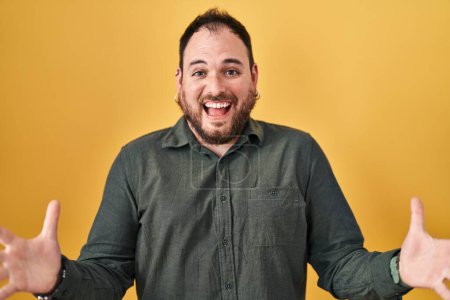 Téléchargez les photos : Plus size hispanic man with beard standing over yellow background celebrating crazy and amazed for success with arms raised and open eyes screaming excited. winner concept - en image libre de droit