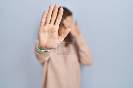 Foto de Mujer joven de pie sobre un fondo aislado cubriendo los ojos con las manos y haciendo un gesto de stop con expresión triste y de miedo. concepto avergonzado y negativo. - Imagen libre de derechos