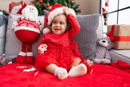 Foto de Adorable chica hispana sonriendo confiada sentada en el sofá junto al árbol de Navidad en casa - Imagen libre de derechos