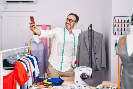 Photo pour Moyen Age homme tailleur sourire confiant faire selfie par smartphone au magasin de tailleur - image libre de droit