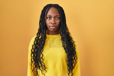 Téléchargez les photos : Femme africaine debout sur fond jaune détendue avec une expression sérieuse sur le visage. simple et naturel regardant la caméra. - en image libre de droit