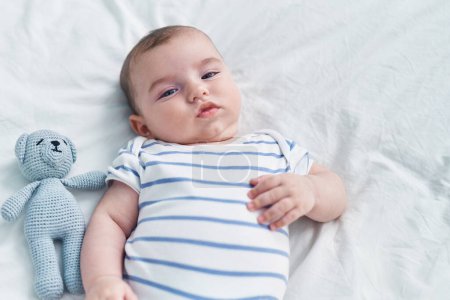 Téléchargez les photos : Adorable bébé caucasien couché sur le lit avec une expression détendue dans la chambre - en image libre de droit