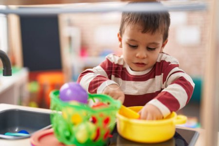 Foto de Adorable niño jugando con la cocina de juego de pie en el jardín de infantes - Imagen libre de derechos