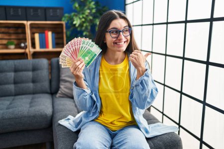 Téléchargez les photos : Young hispanic woman holding norwegian banknotes pointing thumb up to the side smiling happy with open mouth - en image libre de droit