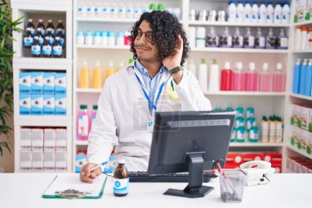 Photo for Hispanic man with curly hair working at pharmacy drugstore smiling with hand over ear listening an hearing to rumor or gossip. deafness concept. - Royalty Free Image