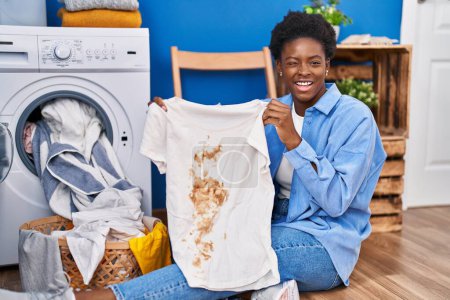 Photo for African american woman holding t shirt with dirty stain winking looking at the camera with sexy expression, cheerful and happy face. - Royalty Free Image