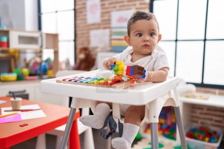 Photo for Adorable hispanic baby sitting on highchair playing xylophone holding car at kindergarten - Royalty Free Image