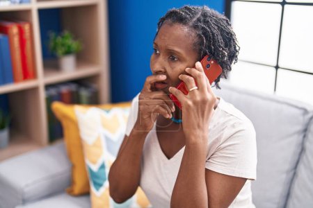 Foto de Middle age african american woman talking on smartphone with worried expression at home - Imagen libre de derechos
