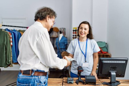 Téléchargez les photos : Middle age man and woman smiling confident paying with dollars at clothing store - en image libre de droit
