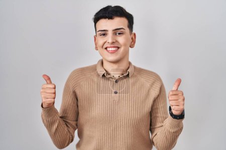 Foto de Non binary person standing over isolated background success sign doing positive gesture with hand, thumbs up smiling and happy. cheerful expression and winner gesture. - Imagen libre de derechos