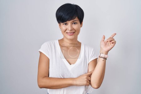 Téléchargez les photos : Young asian woman with short hair standing over isolated background with a big smile on face, pointing with hand finger to the side looking at the camera. - en image libre de droit